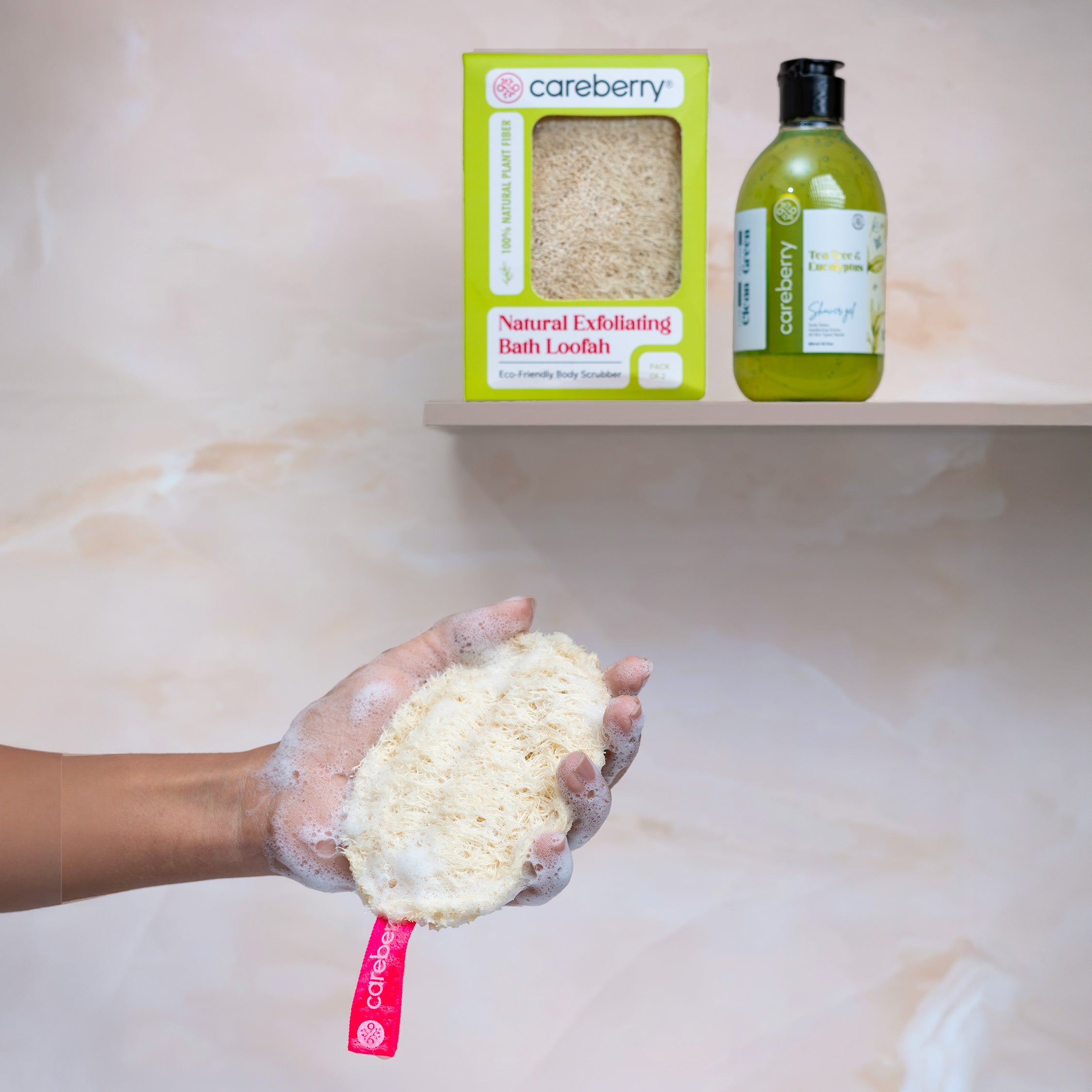 Hand holding foamy Careberry natural bath loofah in shower with green boxed loofah and body wash bottle on shelf in background.